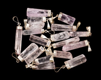 May include: A group of pink crystal pendants with silver bails. The crystals are all different sizes and shapes, but they are all translucent and have a slight pink hue.