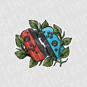 May include: A sticker featuring two video game controllers, one red and one blue, with black buttons. Green leaves and vines surround the controllers, creating a decorative design. The controllers are set against a white background.