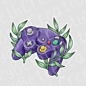 May include: A purple video game controller with a white joystick, a directional pad, and colored buttons. Green leaves surround the controller, creating a decorative design. The controller is a classic gaming accessory.