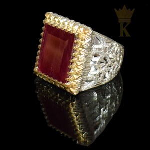 May include: A silver ring with a red gemstone set in a gold-toned frame. The ring has a filigree design.