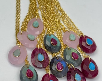 May include: A collection of gold chain necklaces with teardrop-shaped pendants featuring various gemstones. The pendants are made of pink, gray, and red stones with smaller turquoise and ruby accents.