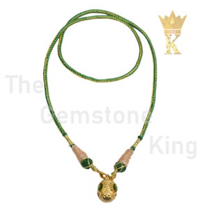 May include: A green and gold cord necklace with a gold pendant shaped like a face. The pendant has green gemstones for eyes.