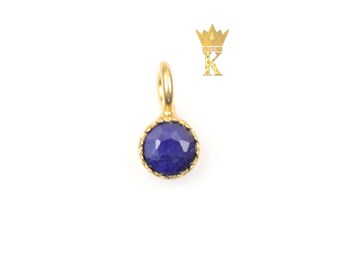 May include: A gold-colored pendant with a round, faceted, deep blue gemstone. The gemstone is set in a gold bezel with a twisted rope design. The pendant has a small loop at the top for a chain.