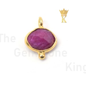 May include: A gold pendant with a pink ruby gemstone. The pendant has a small gold ball at the bottom.
