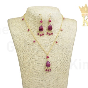 Peut inclure: Un ensemble de collier et de boucles d'oreilles en or avec des gouttes de pierres précieuses rouge rubis pendantes. Le collier a une chaîne plus longue avec un pendentif et une chaîne plus courte avec des pierres plus petites. Les boucles d'oreilles ont une seule grosse goutte de pierre précieuse rouge rubis avec des pierres plus petites qui pendent en dessous.