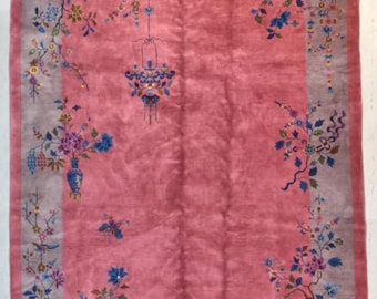 Pode incluir: Um tapete chinês antigo de cor rosa com um design floral. O tapete tem uma borda cinza claro com um padrão floral. O tapete está em bom estado e tem uma textura macia.