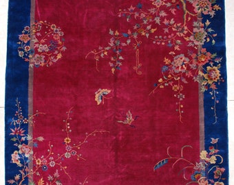 May include: A rectangular rug with a deep red center and a vibrant blue border. The rug features floral and butterfly designs in shades of pink, yellow, green, and blue. The intricate patterns and colors create an elegant and artistic aesthetic.