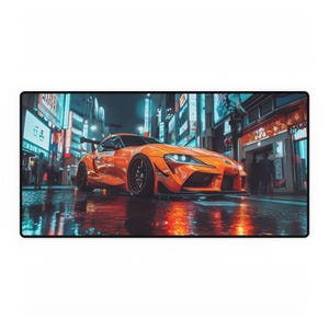 May include: A rectangular desk mat featuring a vibrant orange sports car parked on a wet city street at night. The scene is illuminated by bright neon signs in blue and white, with the car's reflection visible on the damp ground surface.