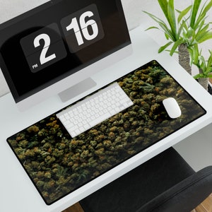 Op de afbeelding: Een groene en bruine muismat met een close-up afbeelding van een dichte cluster van groene knoppen. De muismat ligt op een wit bureau met een computermonitor, toetsenbord en een witte muis.