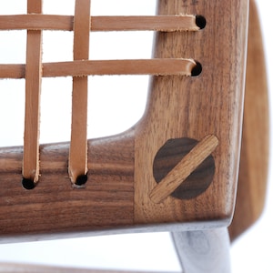 Könnte beinhalten: Nahaufnahme eines Holzstuhls mit einem Ledersitz. Der Stuhl ist aus dunklem Holz gefertigt und hat einen geflochtenen Ledersitz. Der Stuhl ist ein schlichtes Design mit einer geschwungenen Rückenlehne und vier Beinen.