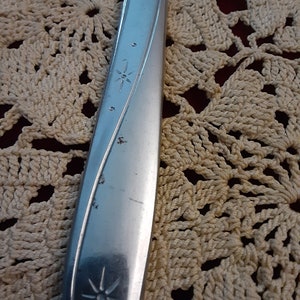 May include: Close-up of a silver knife with a star design on the handle. The knife is resting on a crocheted surface.