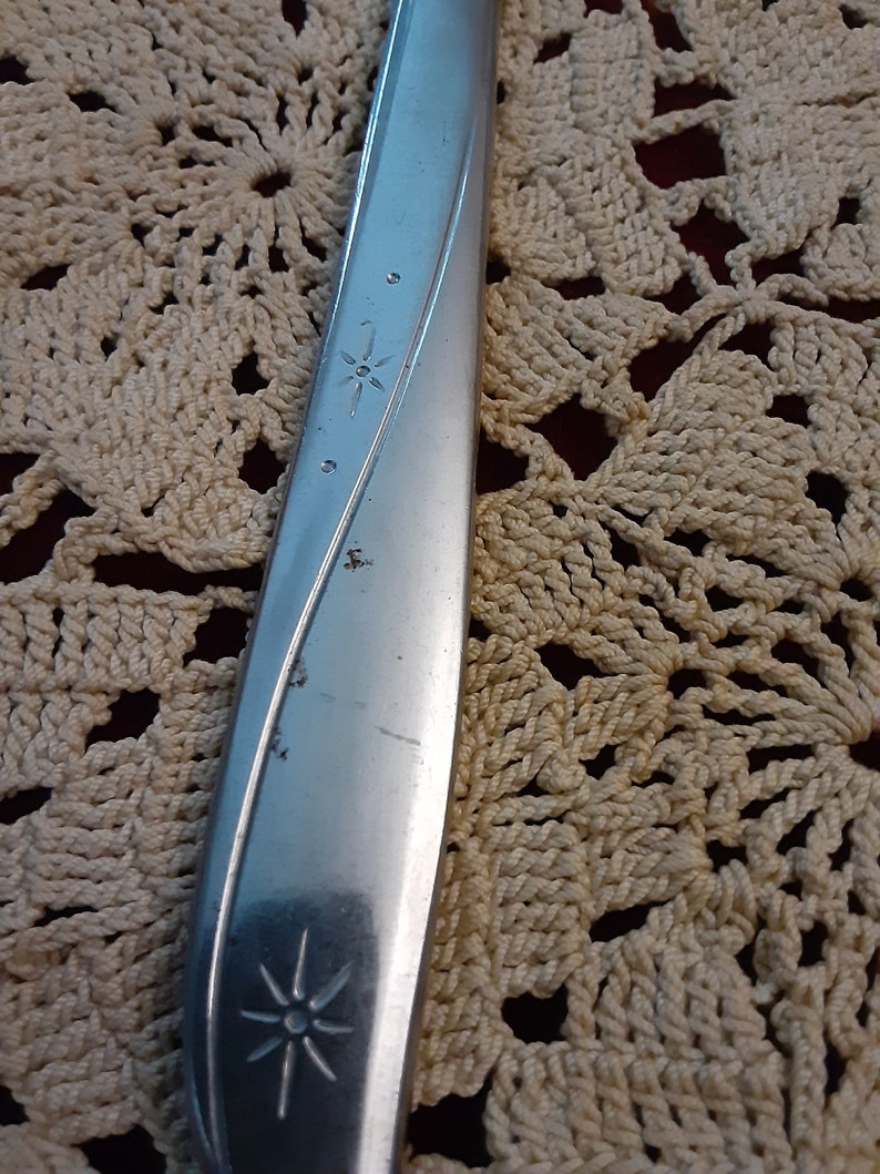 May include: Close-up of a silver knife with a star design on the handle. The knife is resting on a crocheted surface.