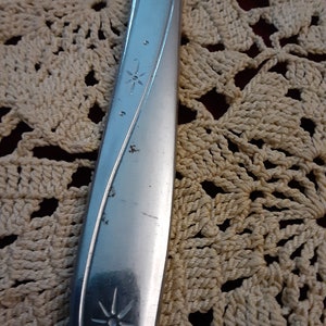 May include: Close-up of a silver knife with a star design on the handle. The knife is lying on a crocheted surface.