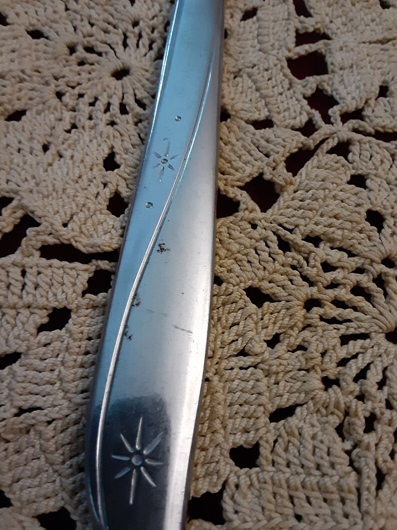 May include: Close-up of a silver knife with a star design on the handle. The knife is lying on a crocheted surface.