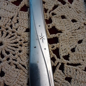 May include: Close-up of a silver knife with a star-shaped design on the handle.