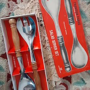 May include: A vintage salad server set in a red box. The set includes a fork and spoon with stainless steel heads and wooden handles. The box reads "Frontier Forge" and "Salad Server Set".