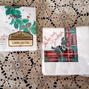 May include: Two packs of Christmas-themed paper napkins. The first pack has a holly and berry design and says "Hallmark Beverage Napkins 16 Napkins (10 in. x 9 1/2 in.)". The second pack has a red and green plaid design with a holly sprig and says "Season's Greetings".