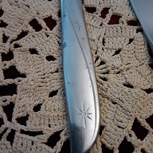 May include: Close-up of a silver knife with a star design on the handle. The knife is lying on a white crocheted doily.