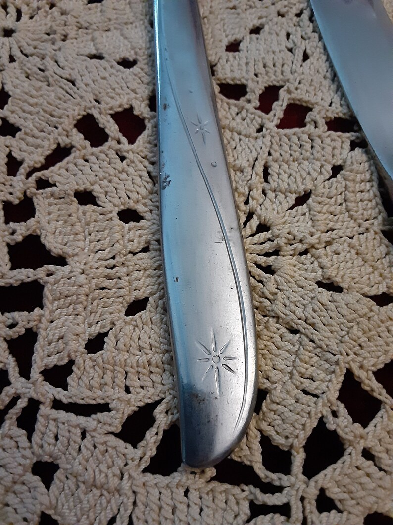 May include: Close-up of a silver knife with a star design on the handle. The knife is lying on a white crocheted doily.