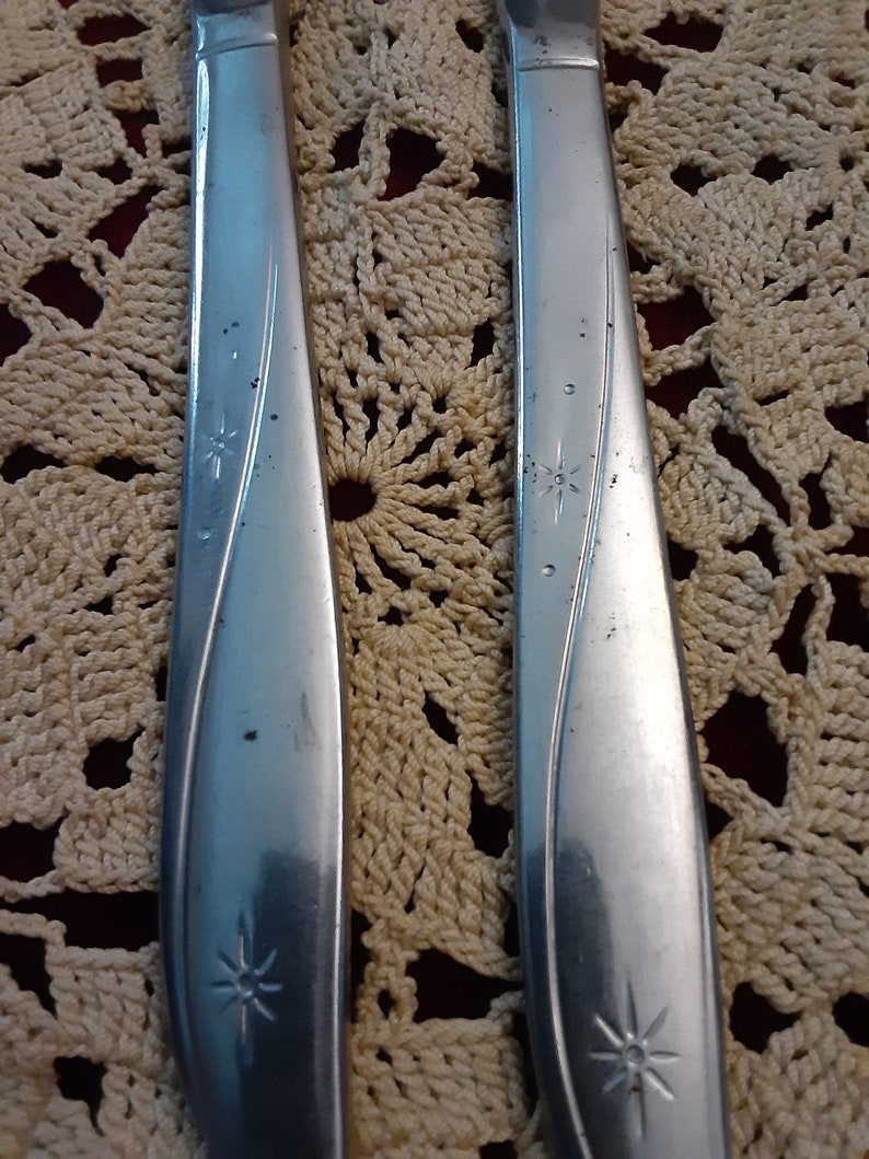 May include: Two silver flatware pieces with a star design on the handle. The flatware is on a crocheted surface.