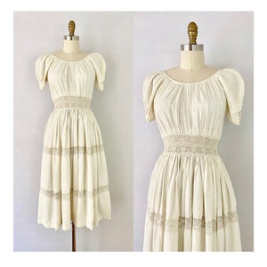 May include: A white vintage dress with a lace trim and puff sleeves. The dress has a fitted bodice and a flowing skirt.