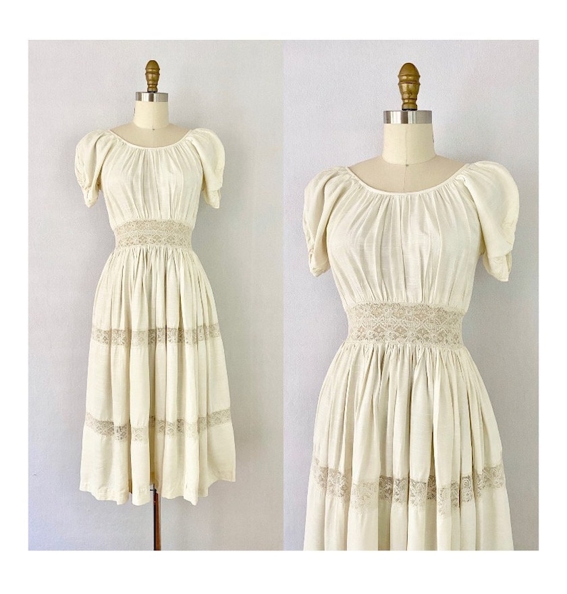 May include: A white vintage dress with a lace trim and puff sleeves. The dress has a fitted bodice and a flowing skirt.
