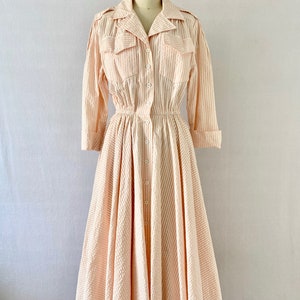 Pu&ograve; includere: Un abito vintage a righe rosa e bianche con chiusura a bottoni, maniche lunghe e gonna ampia. L'abito ha una vita stretta e una vestibilit&agrave; rilassata.