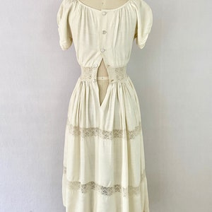 May include: A white vintage dress with a lace trim and a button-up back. The dress has a fitted bodice and a full skirt.