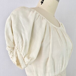 May include: A white, off-the-shoulder dress with puffed sleeves and a lace trim at the waist.