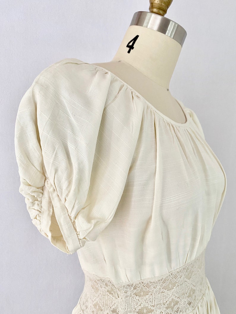 May include: A white, off-the-shoulder dress with puffed sleeves and a lace trim at the waist.