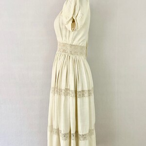 May include: A white cotton dress with a lace trim around the waist and hem. The dress has a fitted bodice and a full skirt.