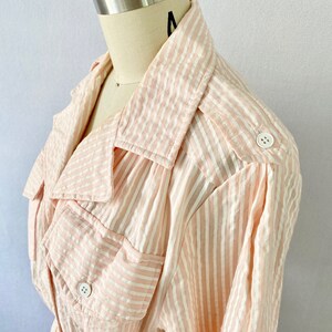 Pu&ograve; includere: Una camicia a maniche lunghe a righe rosa e bianche con colletto e due tasche con bottoni. La camicia ha una vestibilit&agrave; rilassata ed &egrave; realizzata in un tessuto leggero.