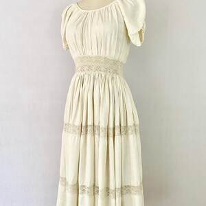 May include: A white vintage dress with a lace trim and a gathered skirt. The dress has a scoop neck and short puff sleeves.