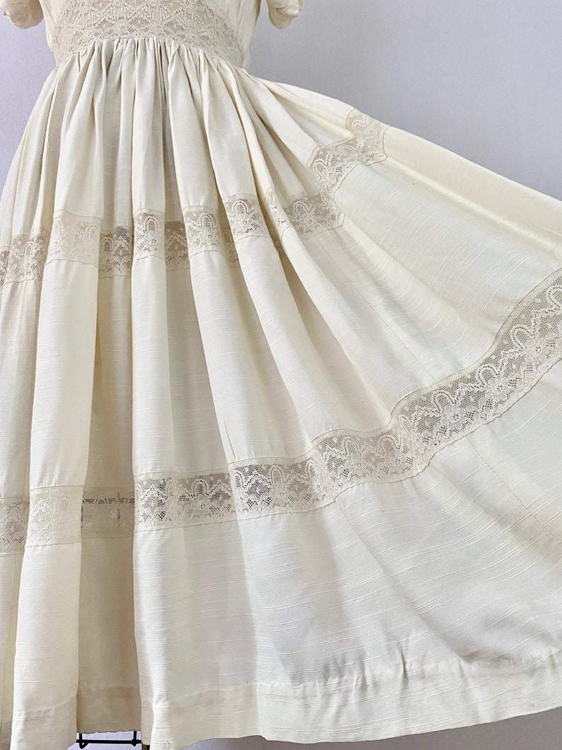 May include: A white cotton dress with a full skirt and lace trim. The dress has a fitted bodice and short sleeves.