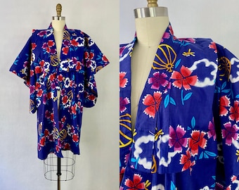 May include: A blue kimono-style robe with a floral pattern. The robe features red, purple, and white flowers, along with yellow and blue accents. The garment is displayed on a mannequin.