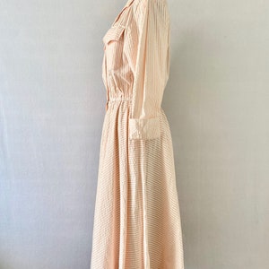 Pu&ograve; includere: Un abito a righe rosa e bianche con maniche lunghe e vita stretta. L'abito ha un colletto e una chiusura con bottoni sul davanti.