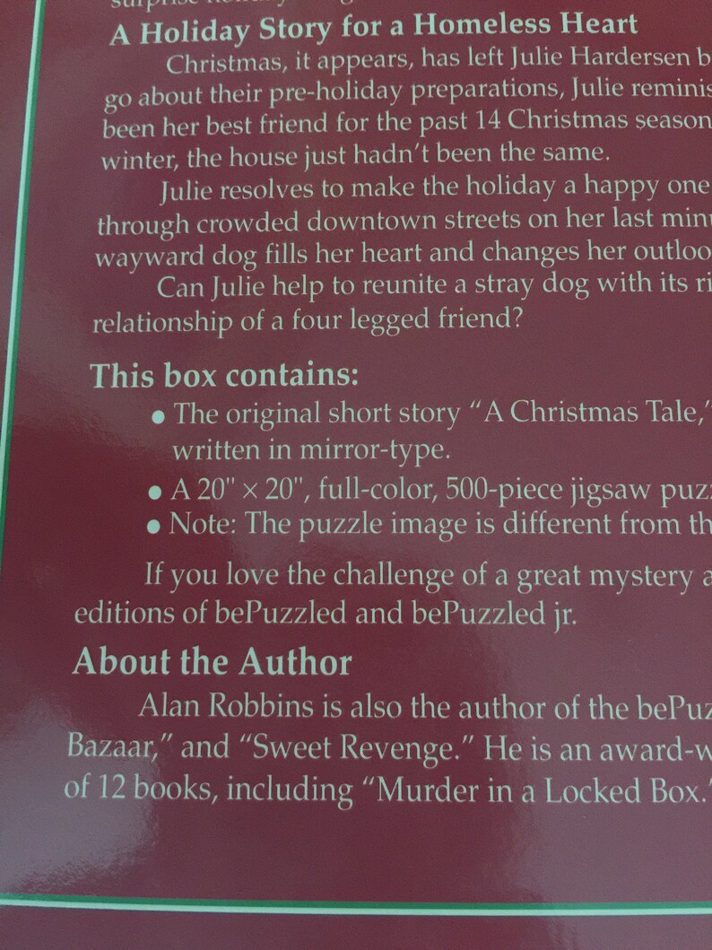 K&ouml;nnte beinhalten: Eine rot-wei&szlig;e Schachtel mit dem Text "A Holiday Story for a Homeless Heart" und einer Beschreibung des Inhalts, darunter eine Kurzgeschichte, ein 50,8 cm x 50,8 cm gro&szlig;es Puzzle und Informationen &uuml;ber den Autor Alan Robbins.