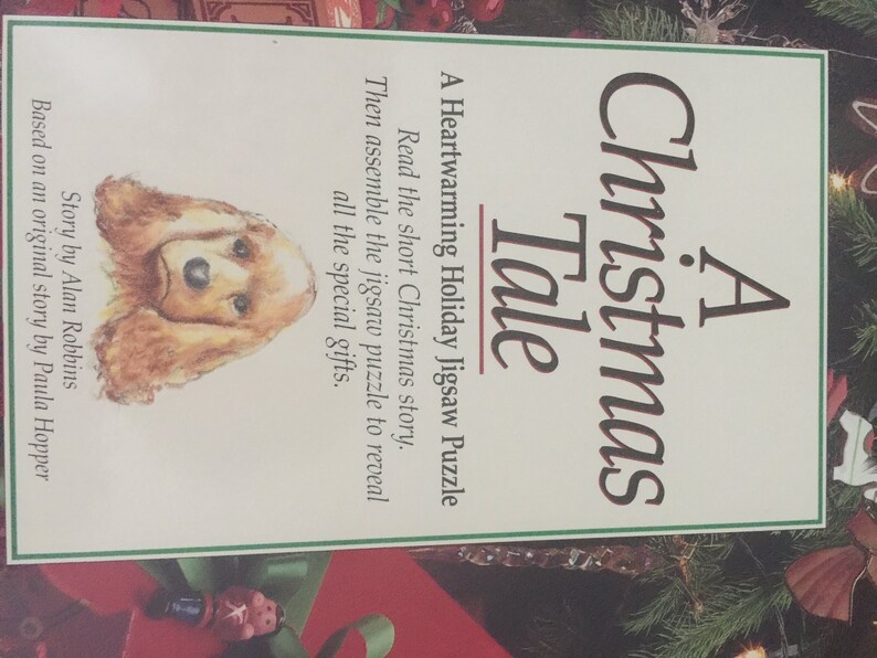 K&ouml;nnte beinhalten: Ein Weihnachts-Puzzle mit dem Titel "A Christmas Tale" mit einer Illustration eines braunen und wei&szlig;en Hundes. Die Puzzlebox hat einen gr&uuml;n-roten Hintergrund mit einem wei&szlig;en Rand.