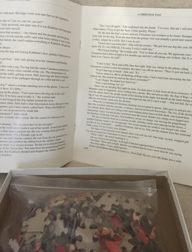 K&ouml;nnte beinhalten: Nahaufnahme eines Buches mit dem Titel "A Christmas Tale" auf wei&szlig;em Hintergrund. Das Buch ist auf einer Seite mit Text &uuml;ber einen verlorenen Hund namens Cinnamon ge&ouml;ffnet. Das Buch liegt auf einer wei&szlig;en Schachtel mit einem durchsichtigen Plastikbeutel, der ein Puzzle enth&auml;lt.