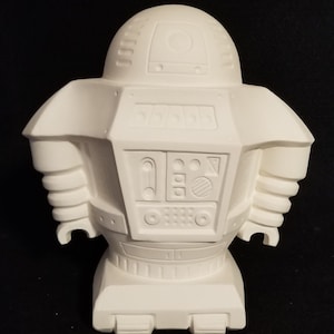 May include: White ceramic robot figurine with a round head and a detailed body. The robot has a variety of buttons and dials on its chest.