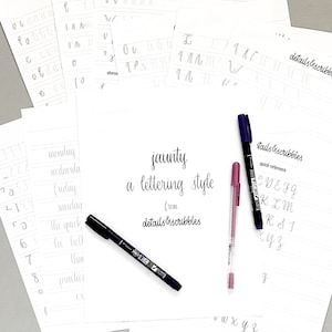 May include: A close-up of a white sheet of paper with the words "jaunty a lettering style from details & scribbles" written in black ink. There are three pens on the paper, one black, one pink, and one blue. The paper is surrounded by other sheets of paper with handwritten letters and words.