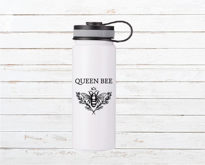 May include: White stainless steel water bottle with a black lid and a black carrying handle. The bottle has a black and white graphic of a bee with a crown on its head and the text "QUEEN BEE".