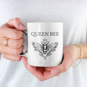 May include: White ceramic mug with a black and white illustration of a bee with a crown and the text "QUEEN BEE".