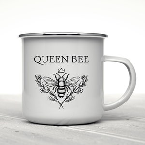 May include: White enamel mug with a black and white illustration of a bee with a crown above it and the text "QUEEN BEE".