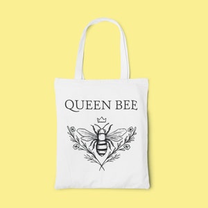 May include: White tote bag with a black and white illustration of a bee with a crown above it and the text "QUEEN BEE" printed on the front.
