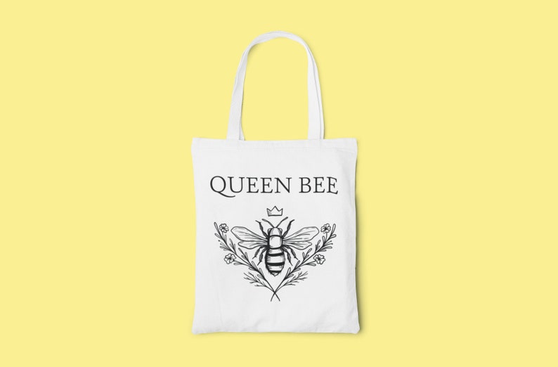 May include: White tote bag with a black and white illustration of a bee with a crown above it and the text "QUEEN BEE" printed on the front.