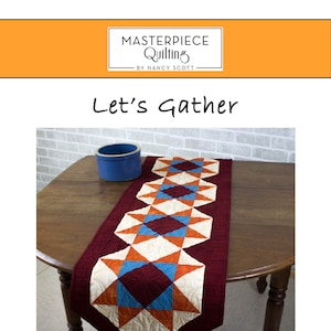 May include: A quilted table runner with a geometric pattern in shades of red, orange, blue, and white. The runner is 16-1/2 inches wide and 72 inches long. The text "Let's Gather" is written above the runner.
