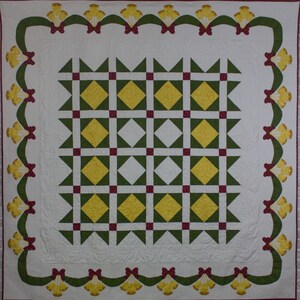 May include: A white quilt with a green and yellow diamond pattern in the centre. The quilt is bordered by a green and red ribbon with yellow bells.