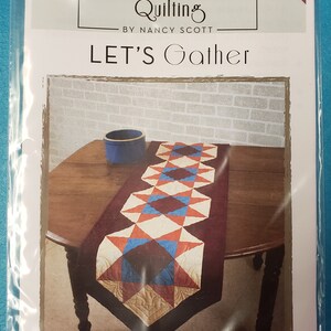 May include: A quilting pattern for a table runner called "Let's Gather" by Nancy Scott. The pattern features a red, blue, and white quilt design with a burgundy border. The finished size is 16 1/2 inches by 72 inches.