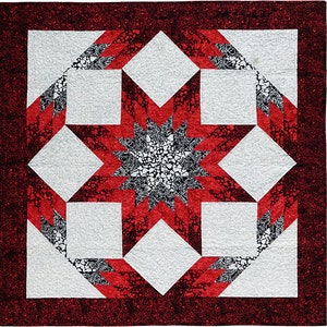 May include: A red and white quilt with a starburst pattern in the center. The starburst is made up of black and white fabric with a heart pattern. The quilt is surrounded by a red border with a black and white pattern.